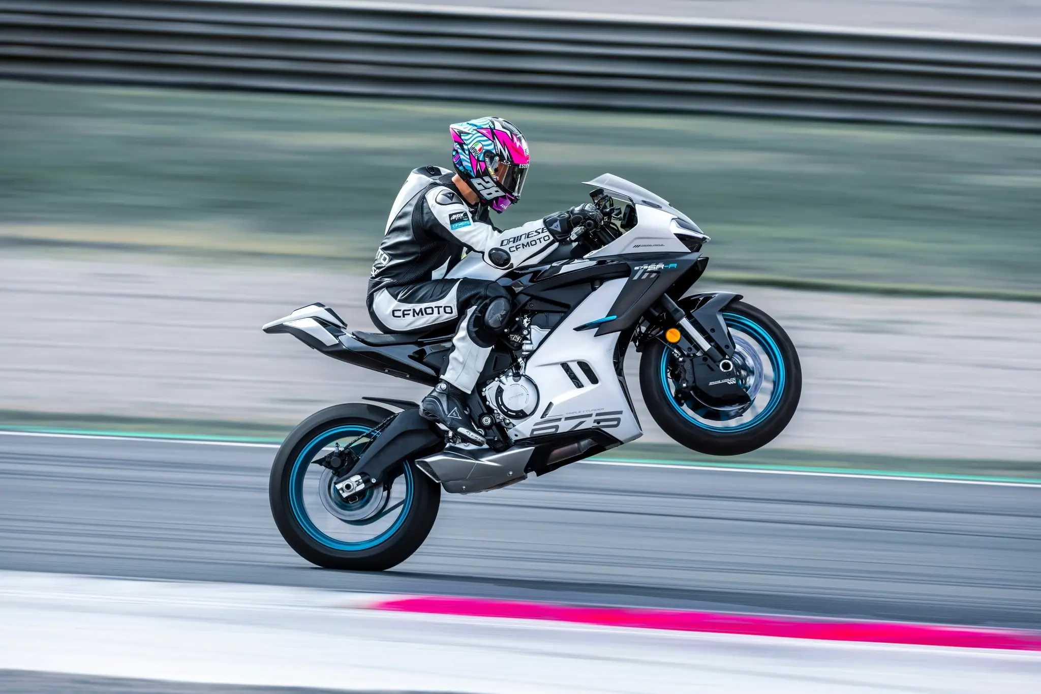 A motorcyclist in full racing gear performs a wheelie on a white 675SR-R CFMOTO sport bike on a racetrack.