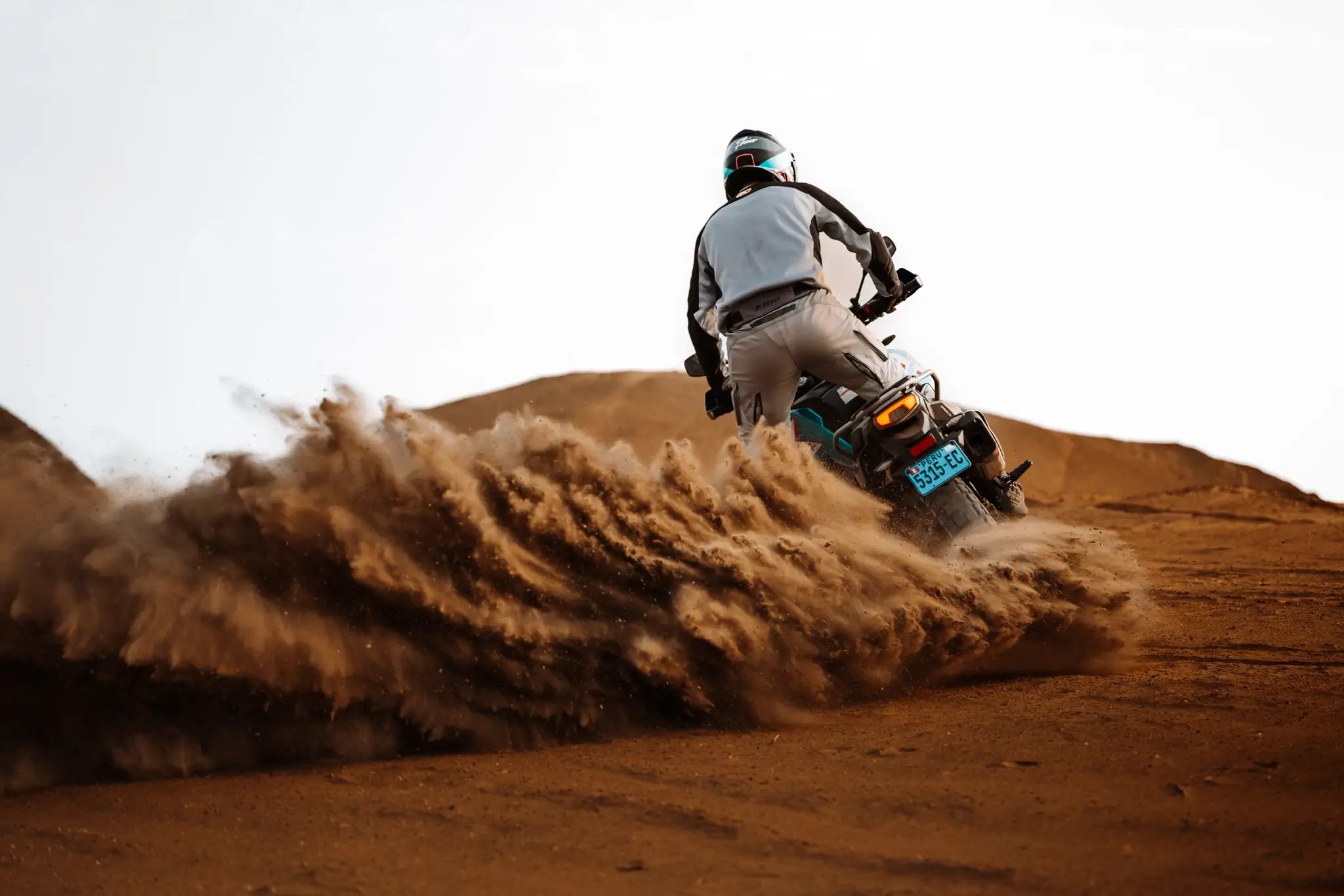 A person wearing protective gear rides an 800MT-X motorcycle on sandy terrain, kicking up a large cloud of dirt behind the bike.