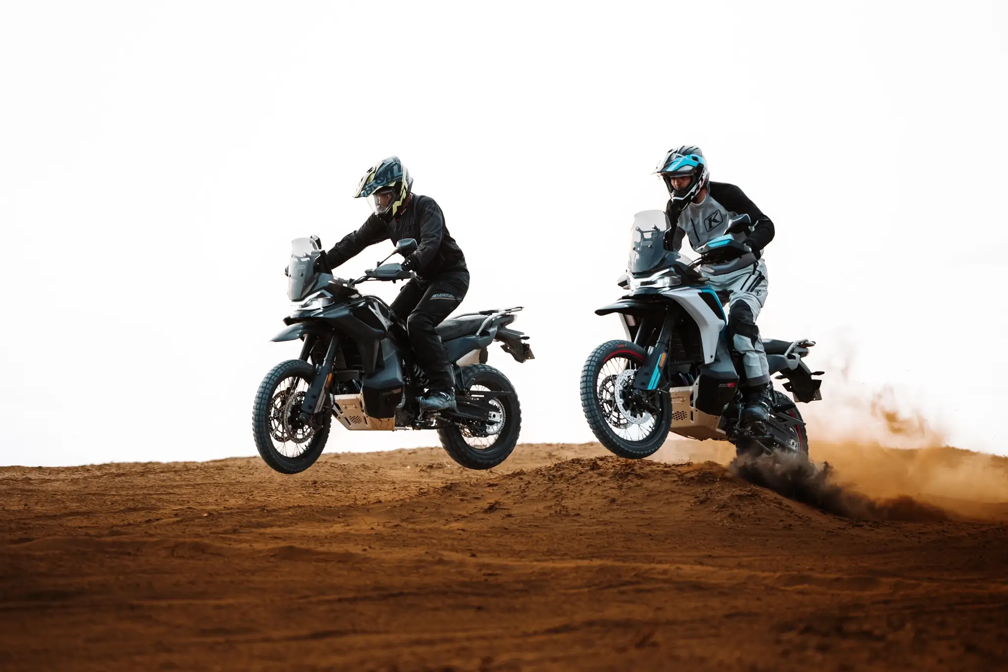 Two people ride 800MT-X adventure motorcycles over a sandy hill, with one airborne and the other kicking up dust as they accelerate.