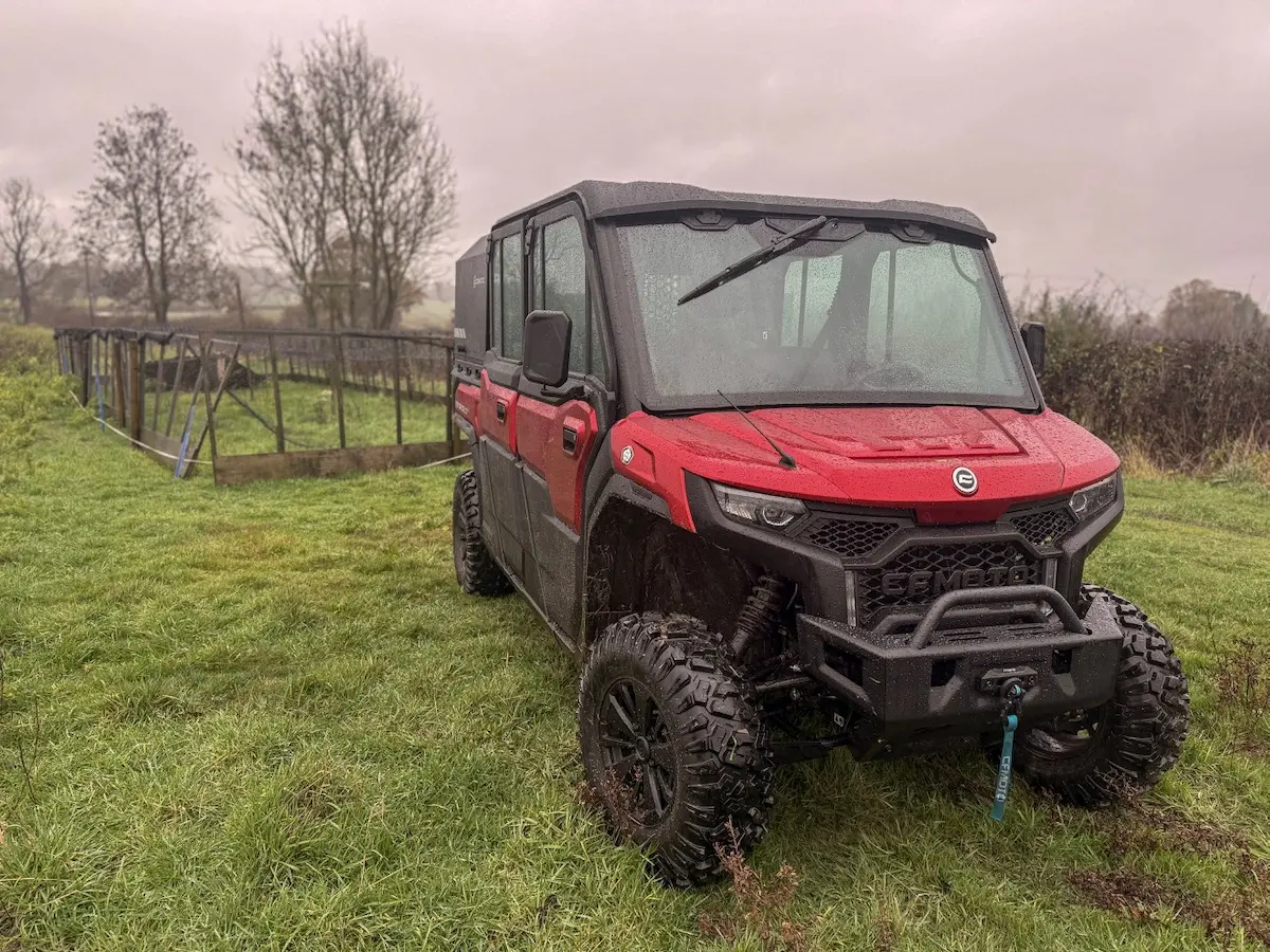 A red UFORCE U10 PRO XL off-road utility vehicle is parked on wet grass near a metal cattle grid on a cloudy, rainy day.