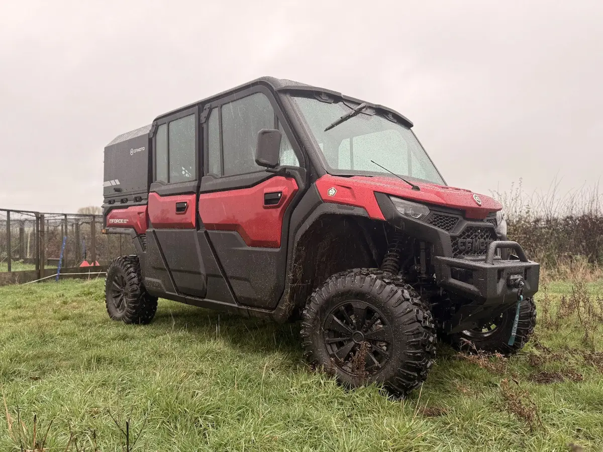 A red and black UFORCE U10 PRO XL off-road utility vehicle with large tires is parked on wet grass in an outdoor setting on a cloudy day.
