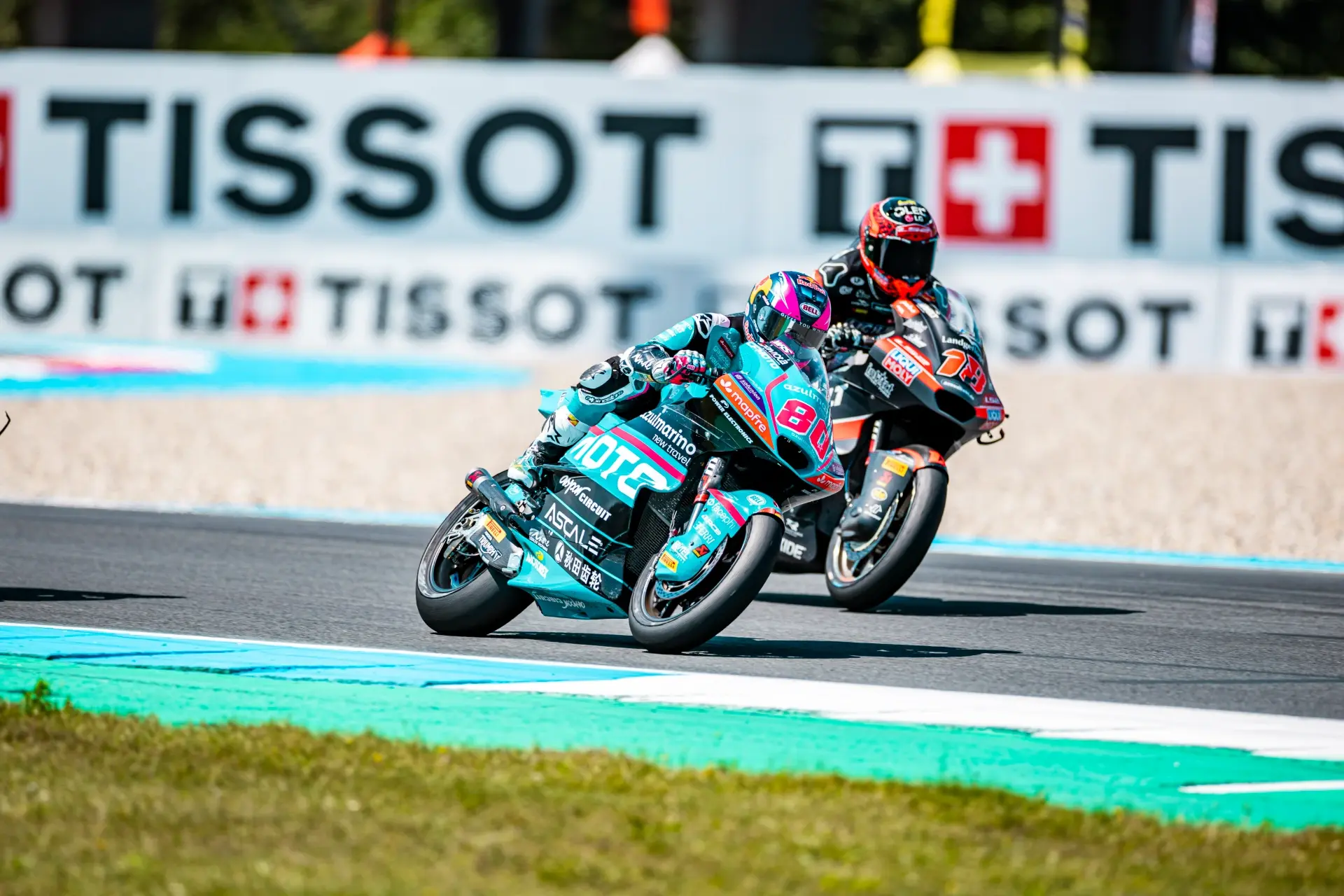 Two motorcycle racers compete on a track at the Dutch MotoGP, leaning into a bend with a Tissot advertisement and CFMOTO branding visible in the background.