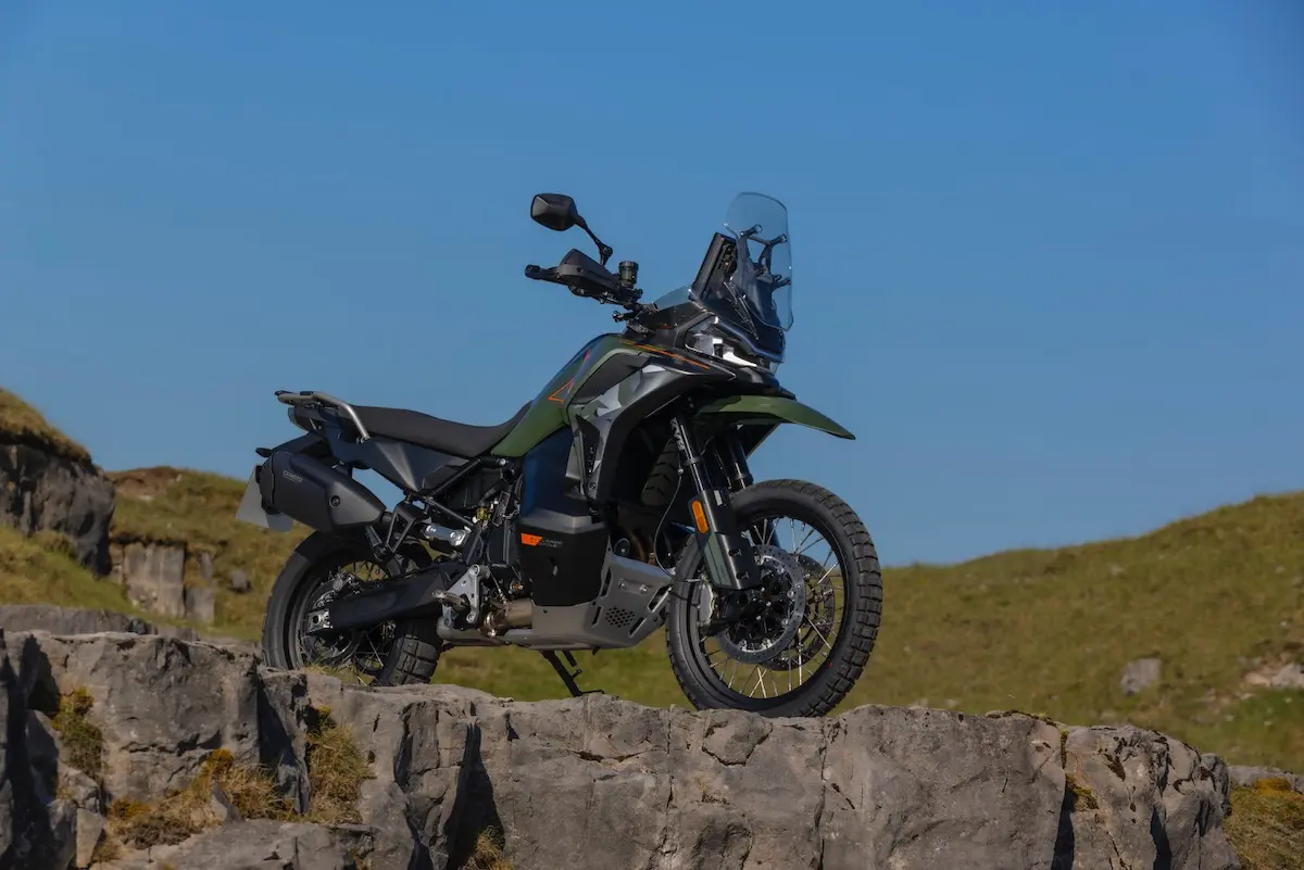 A green and black CFMOTO 1000MT-X adventure motorbike is parked on rocky terrain outdoors under a clear blue sky, ready for exploration—perfect for those seeking a thorough CFMOTO 1000MT-X review in real-world conditions.