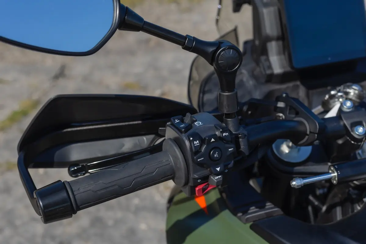Close-up of a CFMOTO 1000MT-X handlebar showing the left-hand grip, control buttons, mirror, and part of the dashboard—perfect for those seeking a detailed CFMOTO 1000MT-X review.