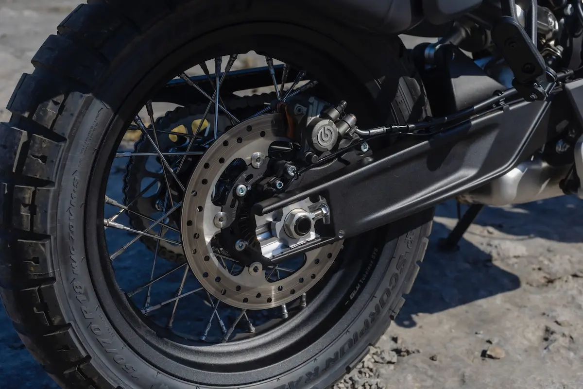 Close-up of a CFMOTO 1000MT-X rear wheel showing the tyre, disc brake, brake calliper, and part of the suspension on a concrete surface—ideal for any CFMOTO 1000MT-X review.