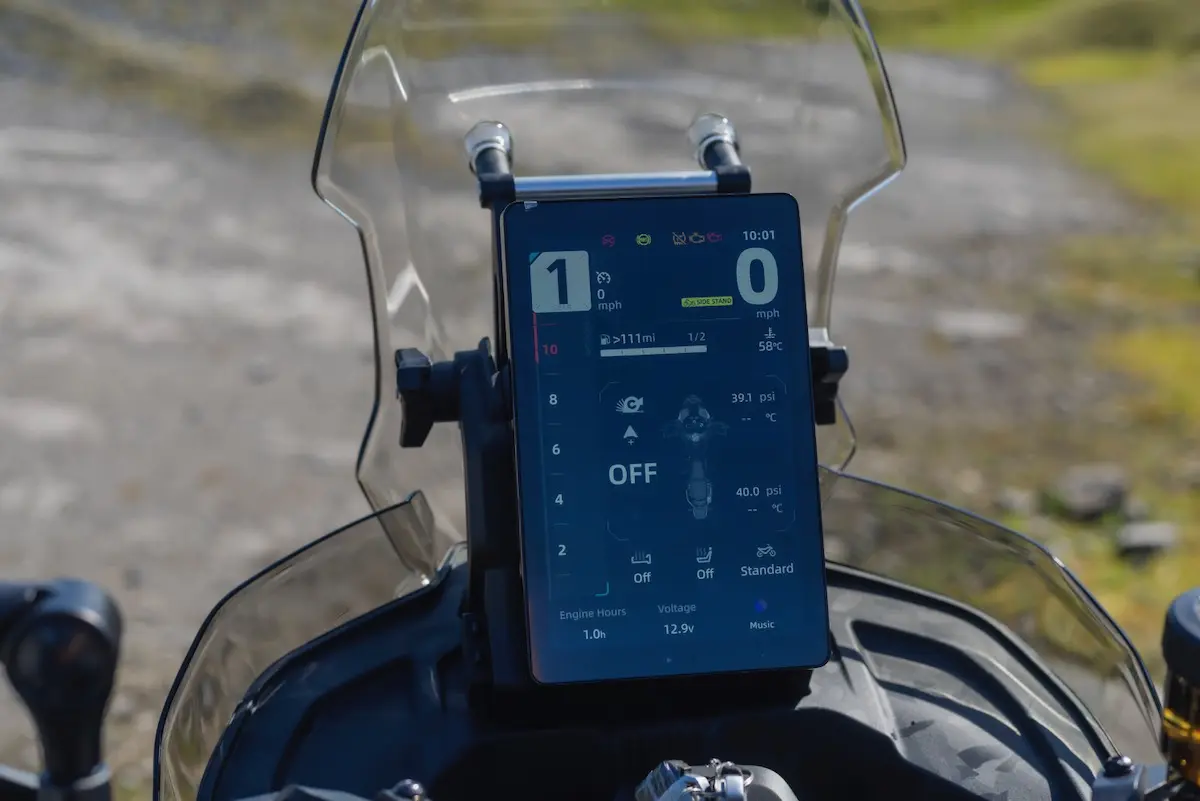 A close-up view of a digital dashboard display on a CFMOTO 1000MT-X, showing speed, gear, tyre pressure, and various system settings, with a blurred outdoor background—perfect for any CFMOTO 1000MT-X review.