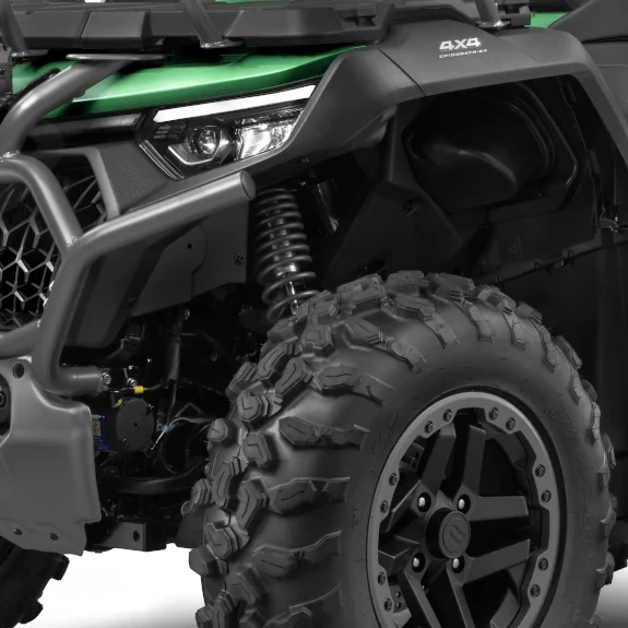 Close-up of the CForce 1000 Touring Premium's front section, showcasing a large, rugged tire, suspension coil, and part of the green body with a headlight.