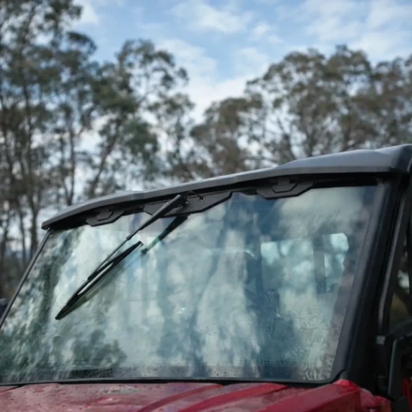 A close-up of a u10 pro agri windscreen with windshield wipers, reflecting trees and clouds in the glass.