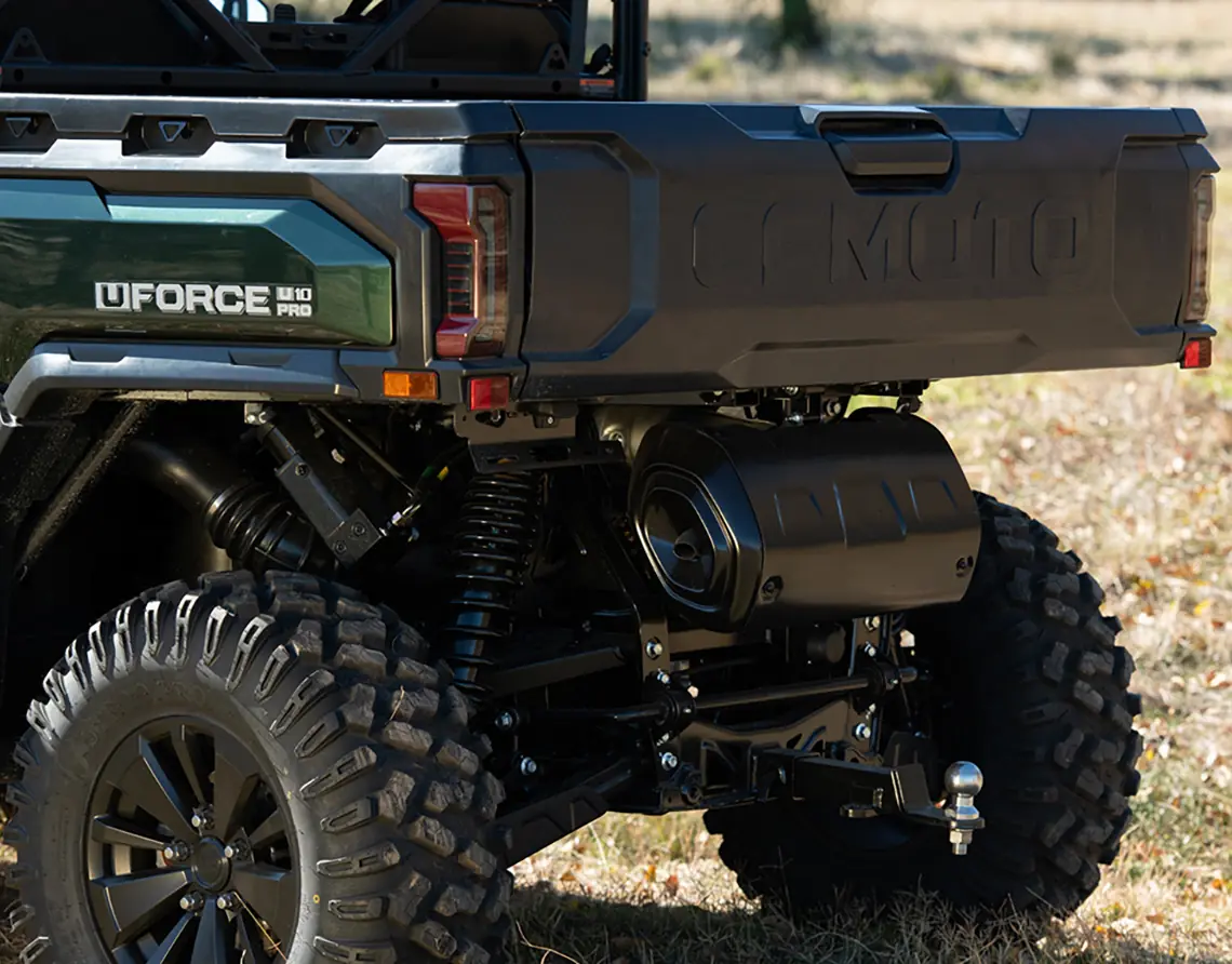 Close-up of the rear section of a green UFORCE 1000 PRO utility vehicle, showcasing ATV technology with its tailgate, suspension, tires, and hitch—ideal for agriculture—in an outdoor setting.