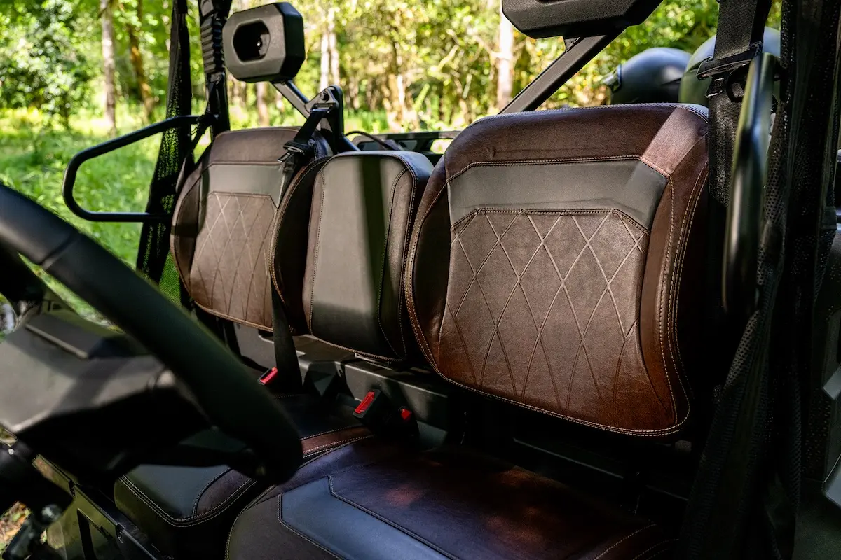 Close-up of brown leather seats with diamond stitching in the UFORCE U10 PRO AGRI off-road vehicle, with greenery visible outside through the windows.