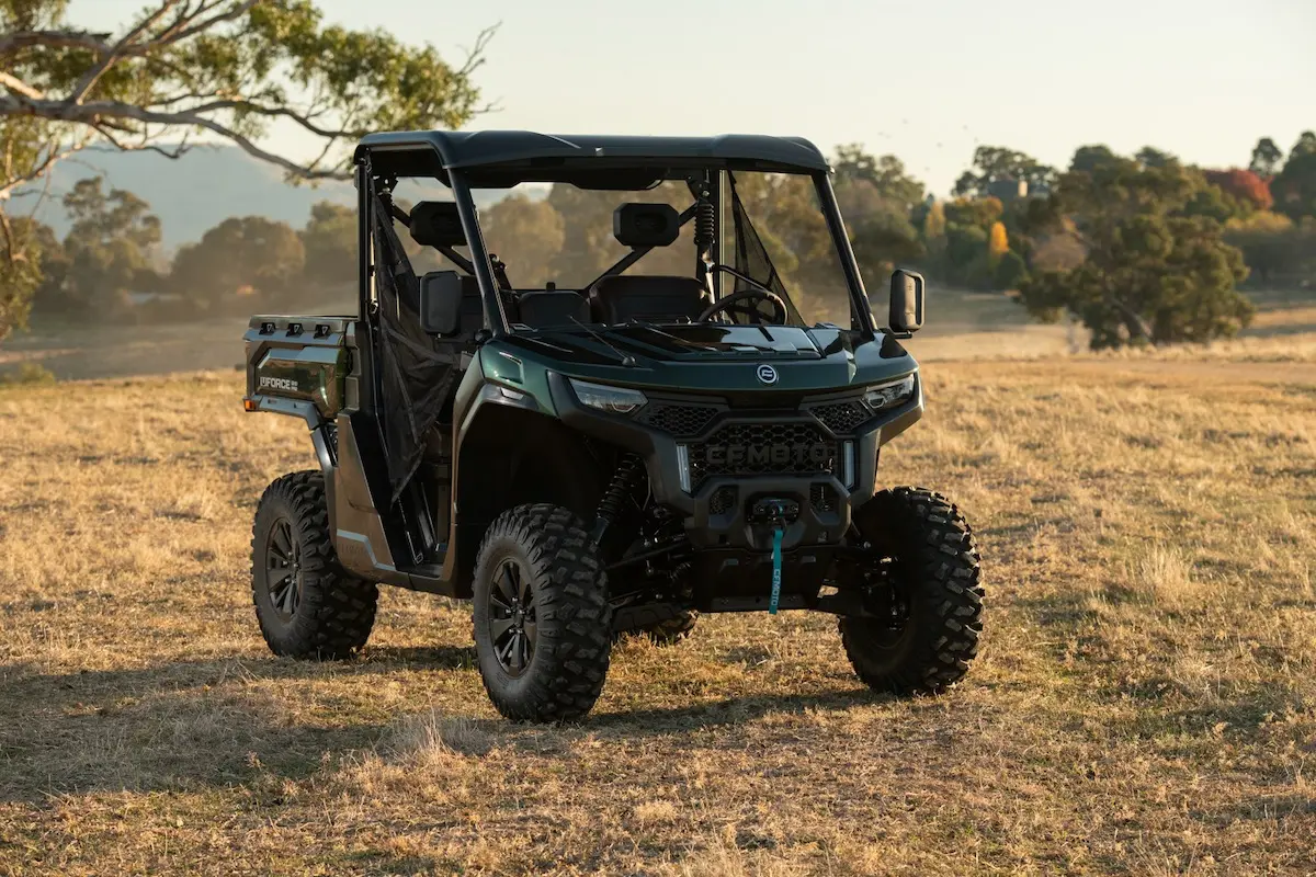 A black UFORCE U10 PRO AGRI side-by-side utility vehicle is parked on dry grass in an open field, with trees and hills visible in the background.