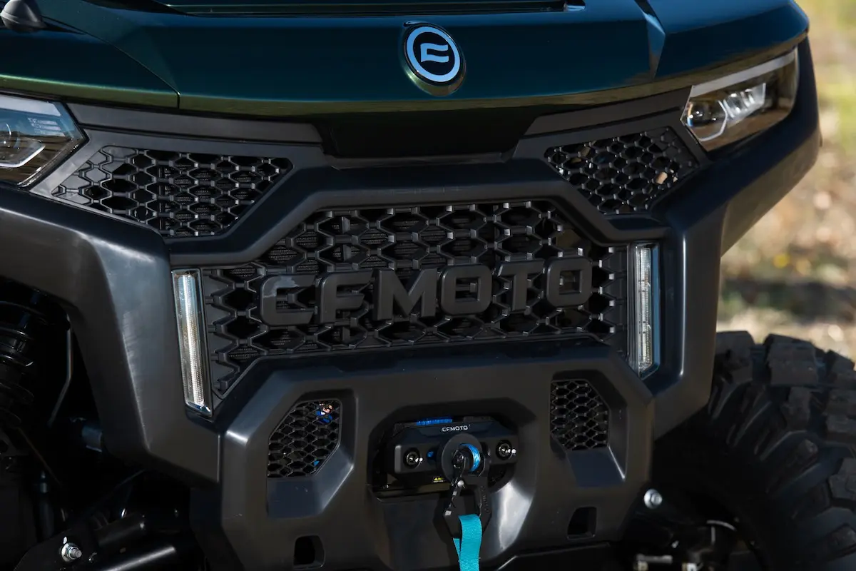 Close-up view of the front grille of a CFMOTO UFORCE U10 PRO AGRI vehicle, featuring the brand logo, bold grille design, and a winch with a distinctive blue strap.