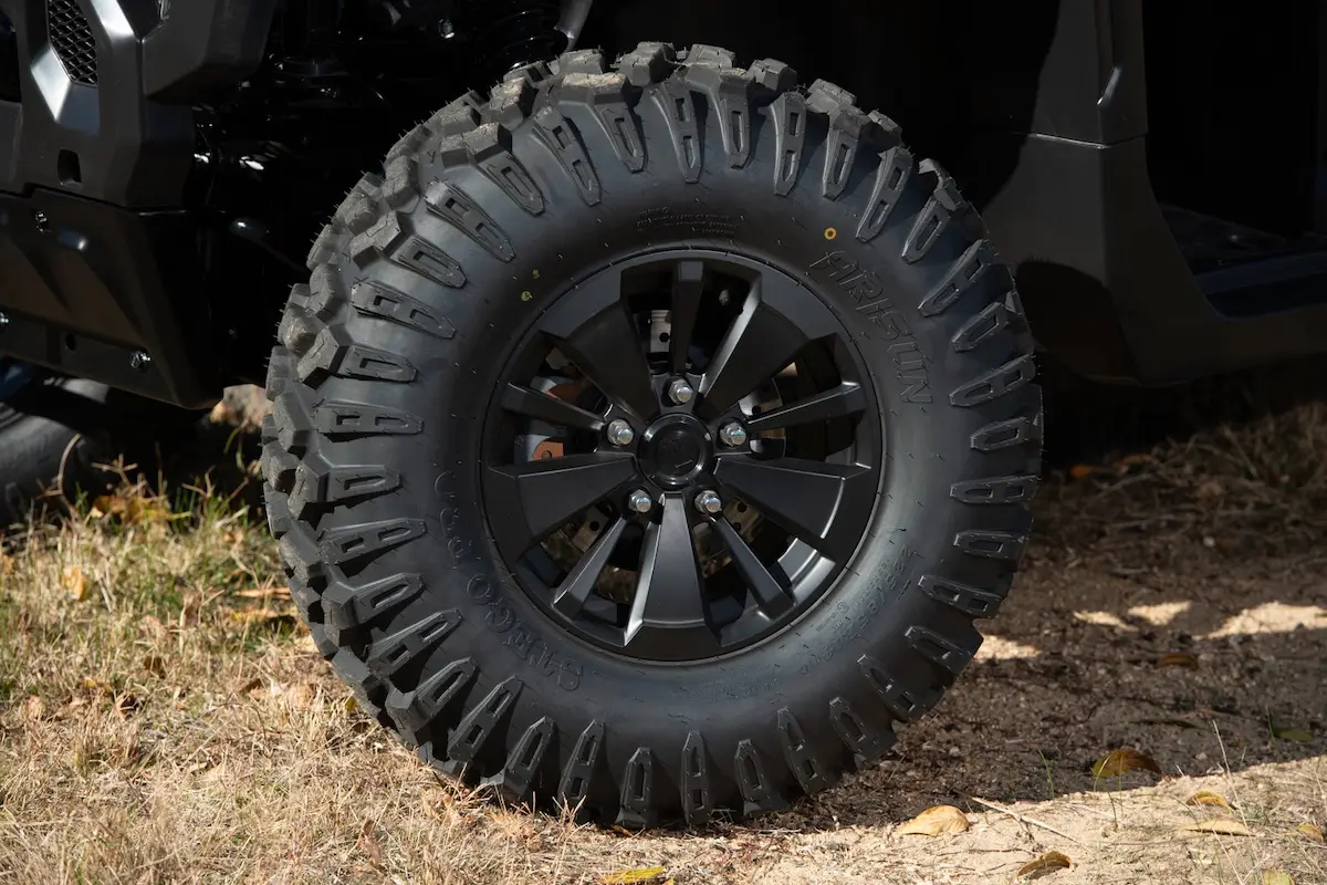 Close-up of a large UFORCE U10 PRO AGRI off-road vehicle tire with deep treads, mounted on a black alloy wheel, parked on dirt and grass.