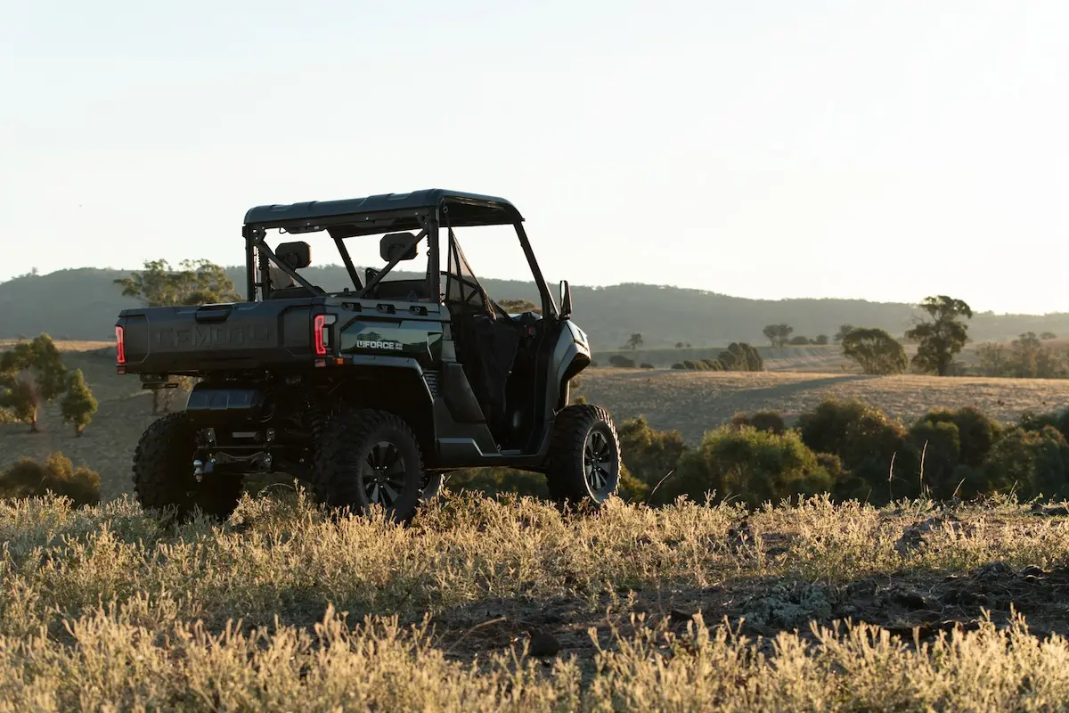 A UFORCE U10 PRO AGRI side-by-side utility vehicle is parked on a grassy hill, overlooking a rural landscape with trees and rolling hills in the background.