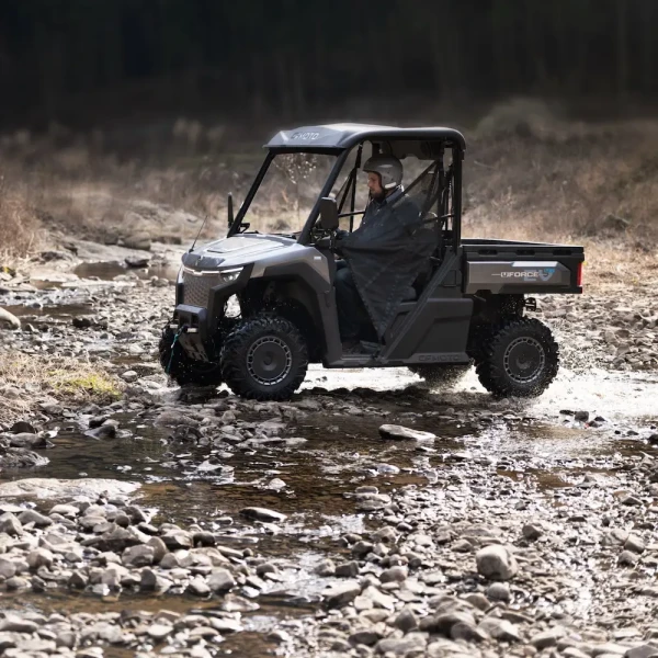 A person drives a black UFORCE EVU6 Commercial side-by-side utility vehicle across a rocky creek bed in an outdoor, rural setting.