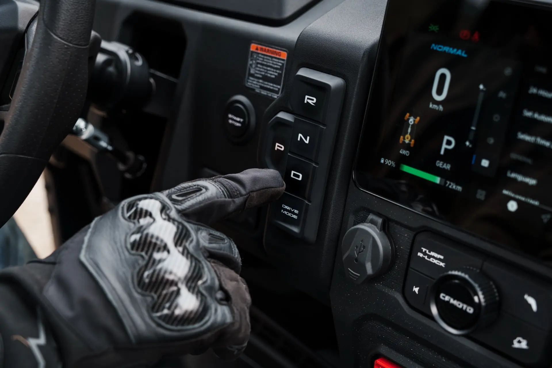 A gloved hand presses the “P” button on a vertical gear selector panel next to a digital dashboard in a UForce 600 vehicle.