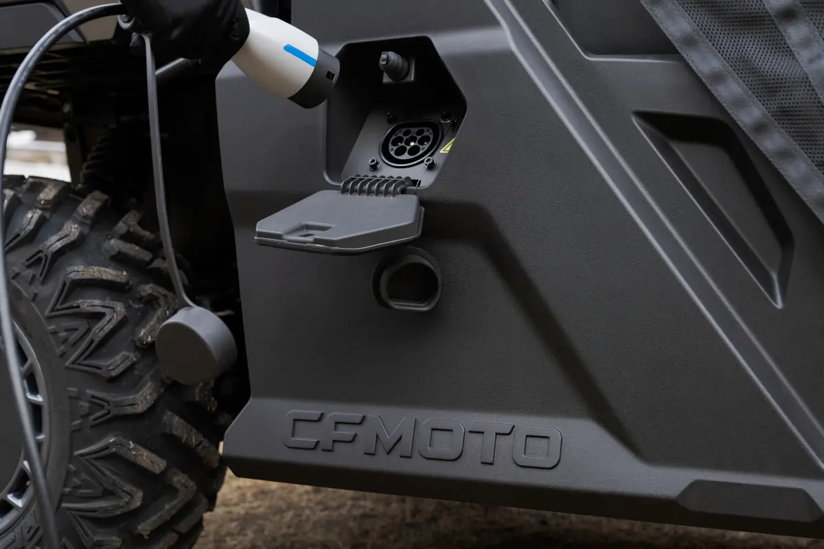 A close-up of a CFMOTO electric UTV being charged, showing the charging port and connector plugged into the side of the vehicle.
