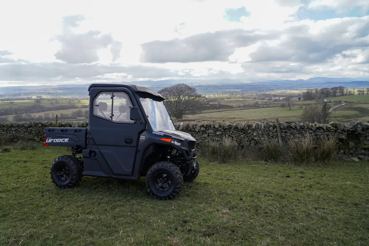 A black UForce 600 utility terrain vehicle is parked on grass in front of a stone wall, with rolling countryside and cloudy skies in the background.