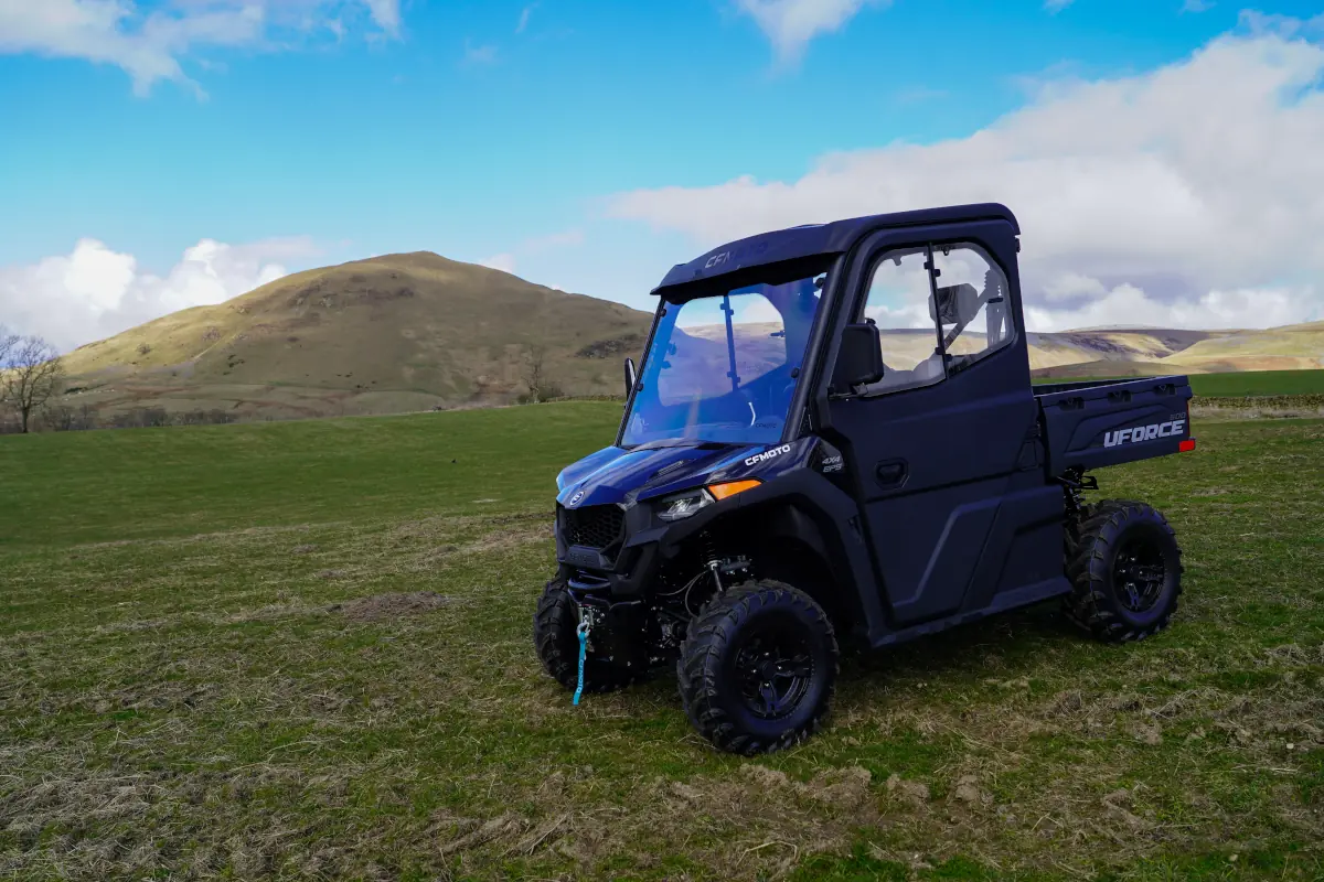 A black UTV utility vehicle, the UFORCE 600, is parked on grassy terrain with hills and a partly cloudy blue sky in the background.