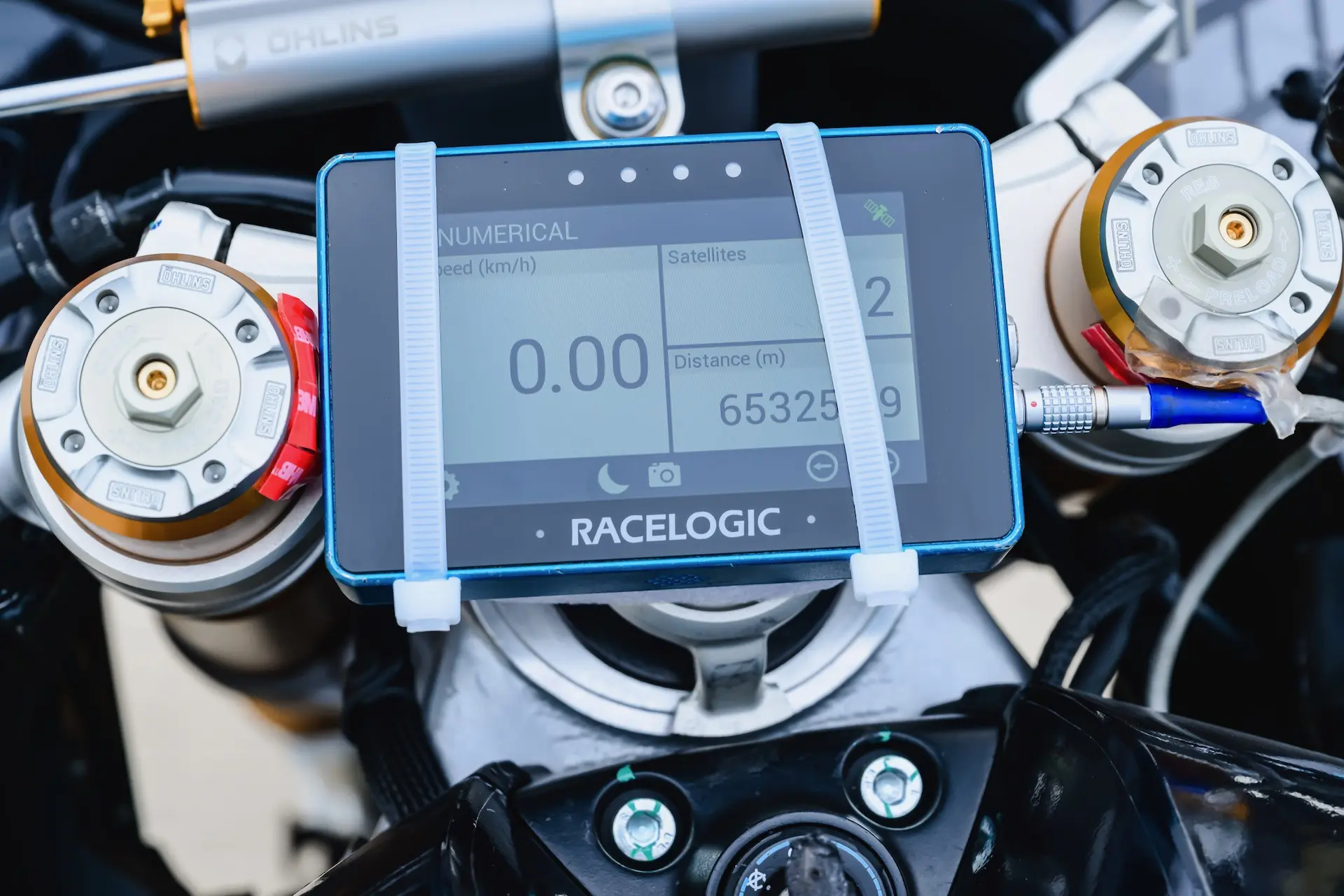 A RACELOGIC digital display mounted on a CFMOTO V4 SR-RR dashboard shows numerical speed, top speed, satellites, and distance data, secured with two white straps.