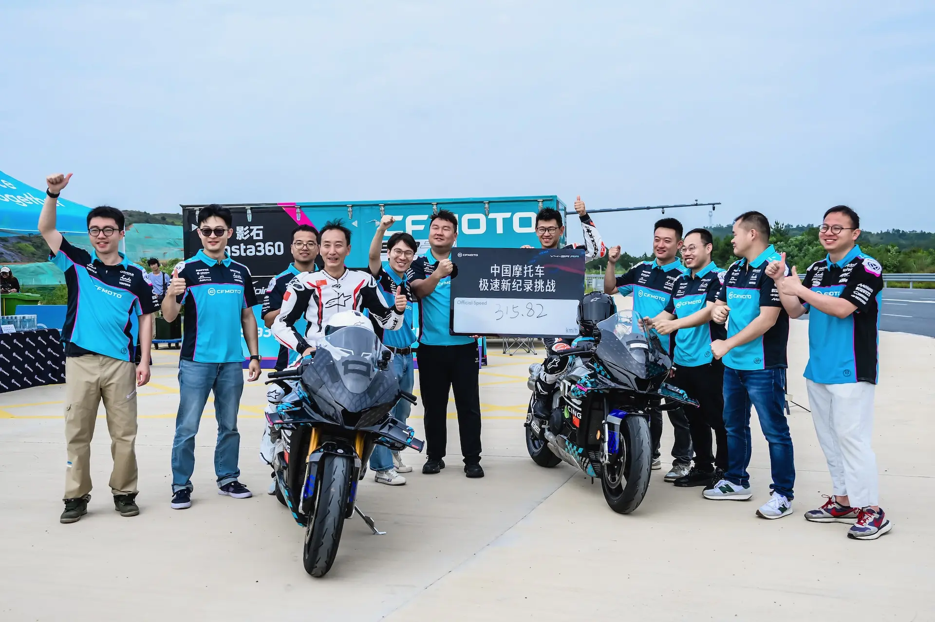 A group of people in matching blue and black shirts pose with two motorbikes outdoors; one person holds a sign with Chinese text and numbers, celebrating the CFMOTO V4 SR-RR and its top speed of 315.82 km/h.